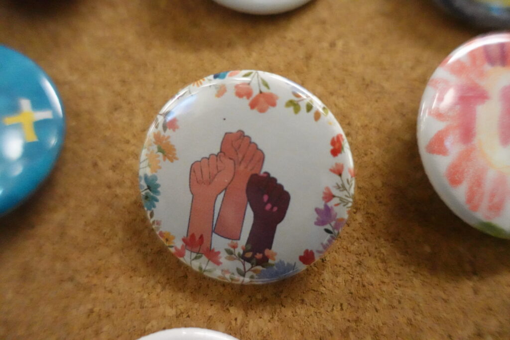A handmade button showing three fists surrounded by flowers raised in solidarity