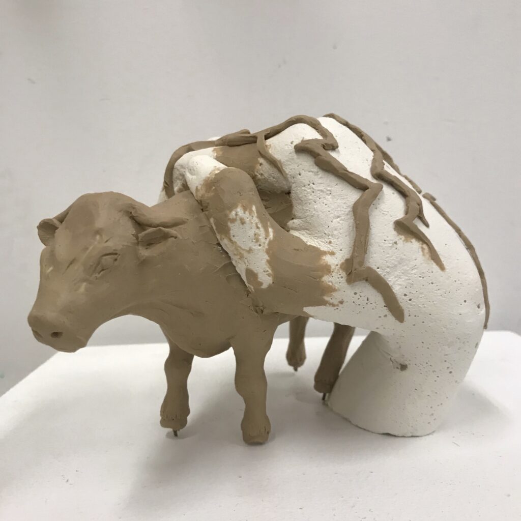 Photograph of a sculpture of a plasticine cow held by a hand on the cow's back.
