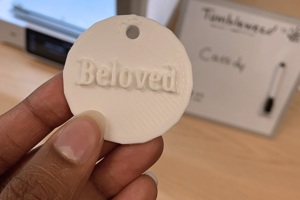 Hand holding a white 3D printed token that reads "Beloved"